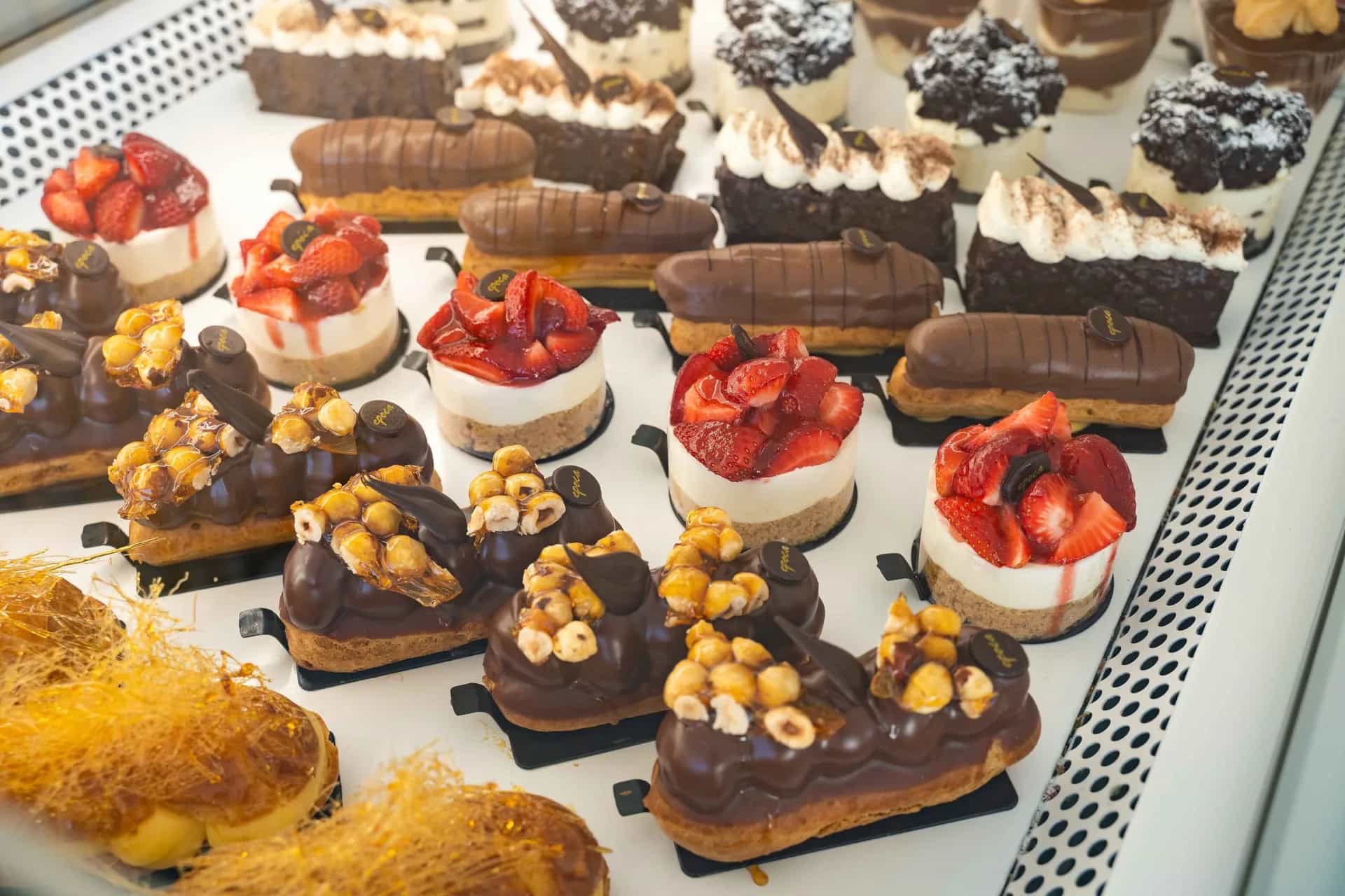 Display case at Epoca Patisserie in Mykonos filled with chocolate éclairs, strawberry tarts and fresh cream pastries