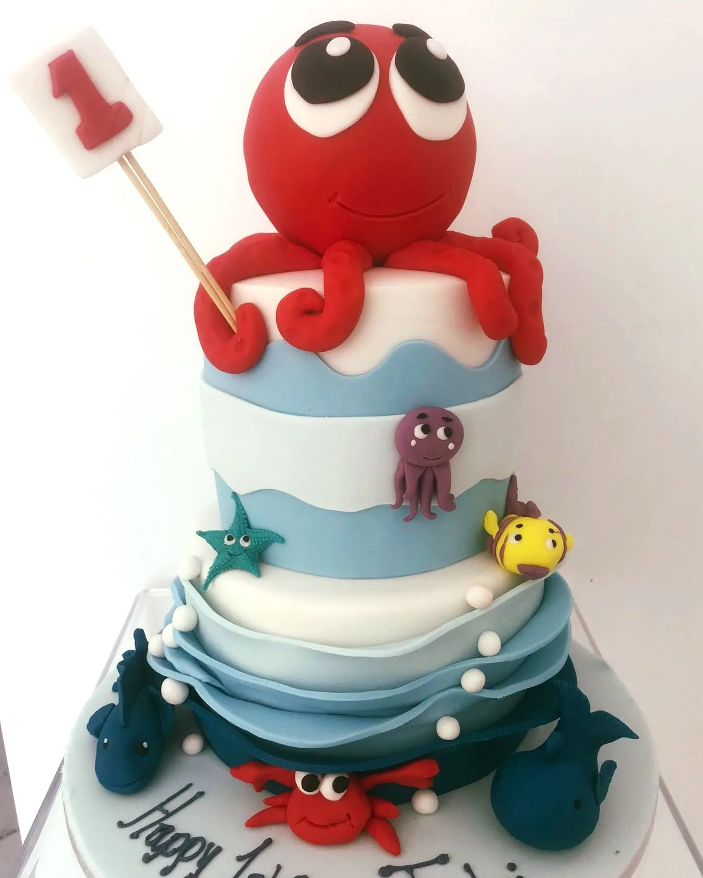 Two-tier under-the-sea children's birthday cake with a sculpted octopus, starfish and sugar waves