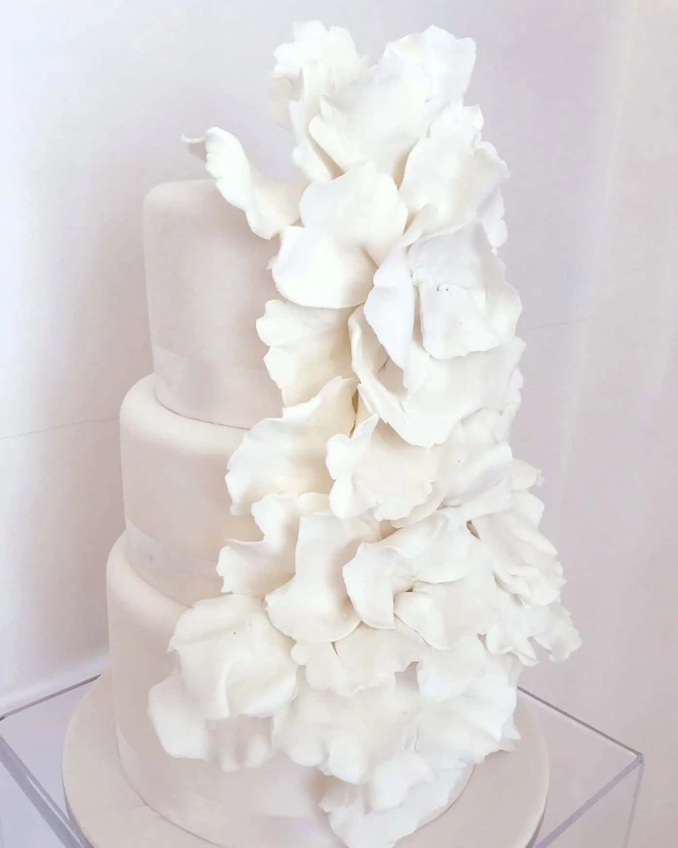 Three-tier white wedding cake with a cascade of handmade sugar petals, created by Epoca Patisserie in Mykonos